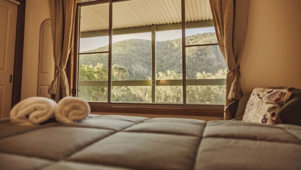 Un dormitorio con un ventanal grande, una cama con cabecera y vistas a una colina boscosa.