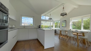 Una cucina moderna con mobili bianchi, un'isola centrale e un'area pranzo con tavolo e sedie in legno.
