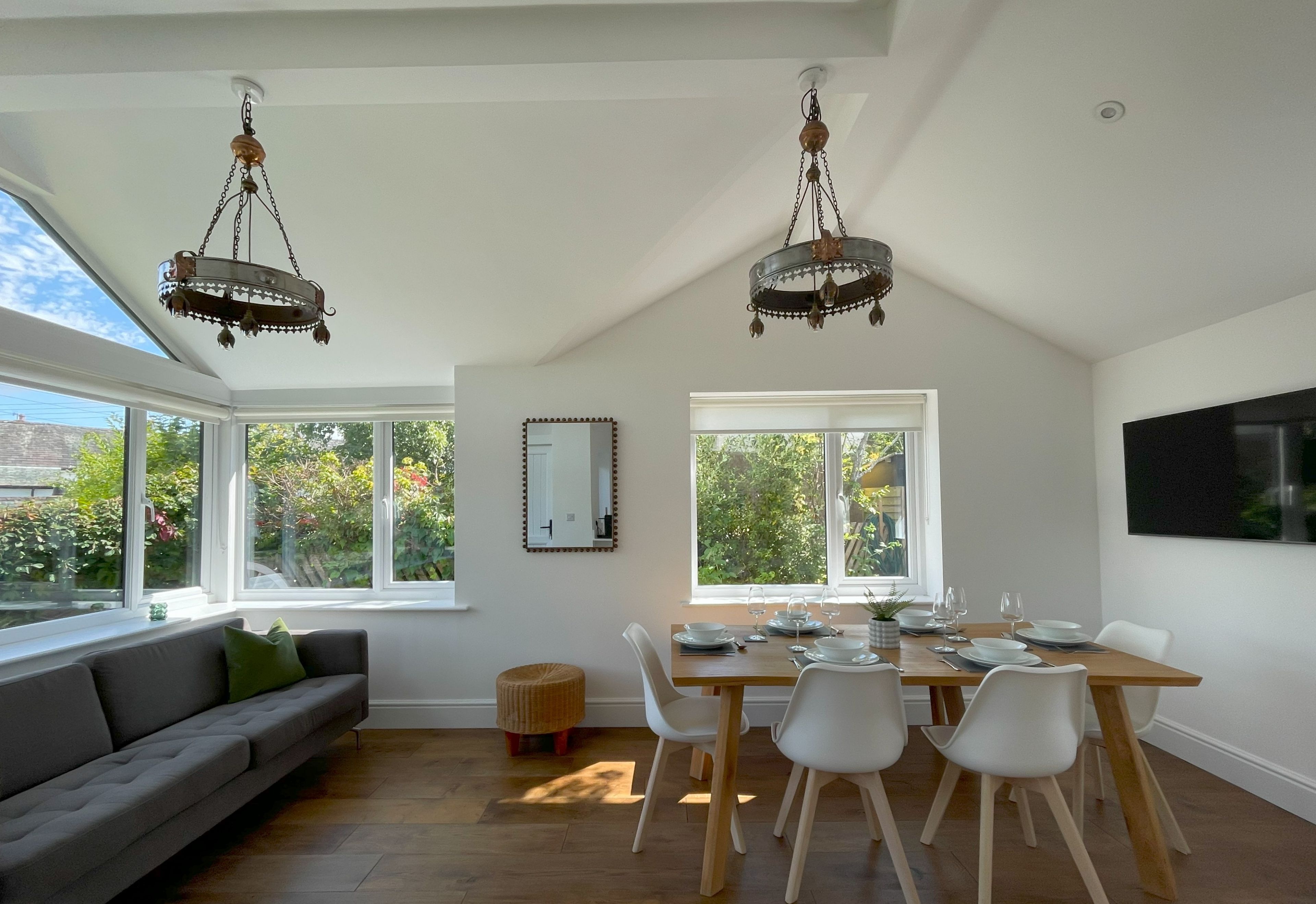 A dining area with a table set for four, a sofa, and two hanging chandeliers.