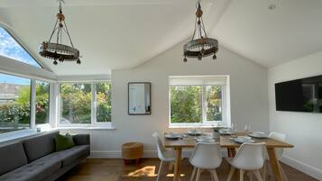 A dining area with a table set for four, a sofa, and two hanging chandeliers.