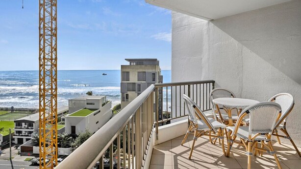 A balcony with wicker chairs and a view of the ocean and buildings. - Carrington Family Beach Getaway - Ocean View, WiFi (Main Beach)