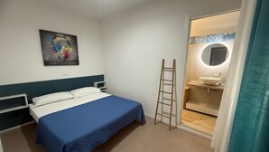 A hotel room with a bed, a bedside table, a mirror, and a bathroom visible through an open door.