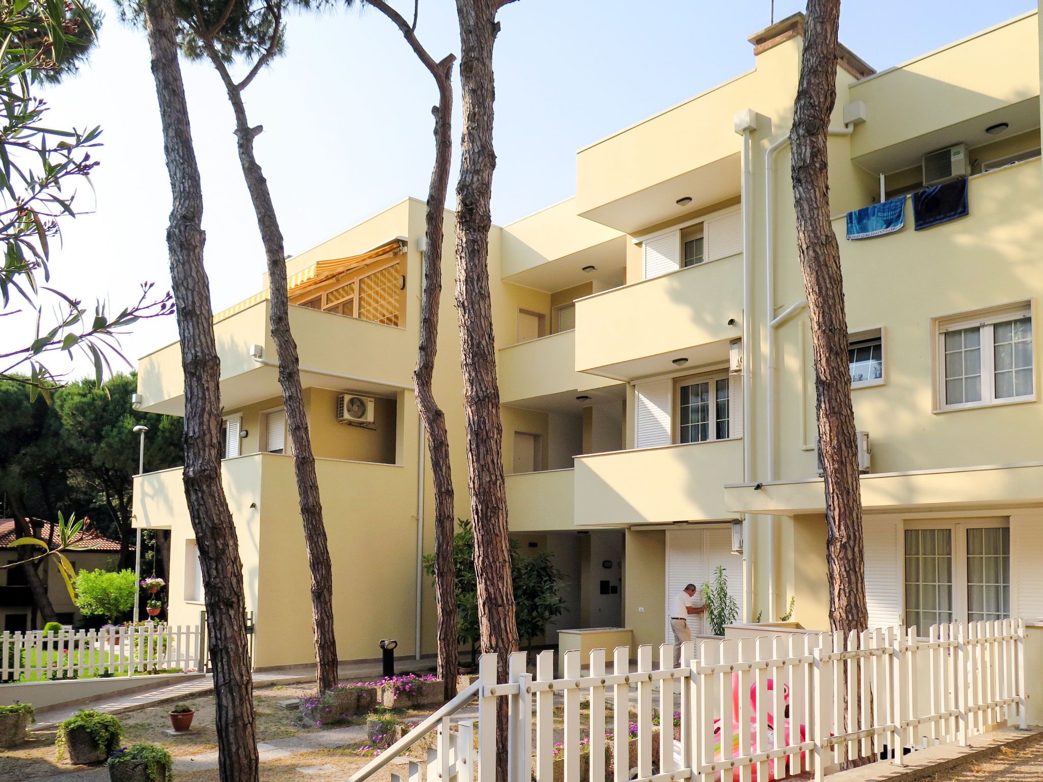 Un hôtel à plusieurs étages doté de balcons, d’une clôture blanche en bois et de plantes en pot.