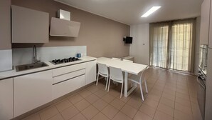 A modern kitchen with a gas stove, sink, and white cabinets. There is a dining table with chairs and a TV mounted on the wall.