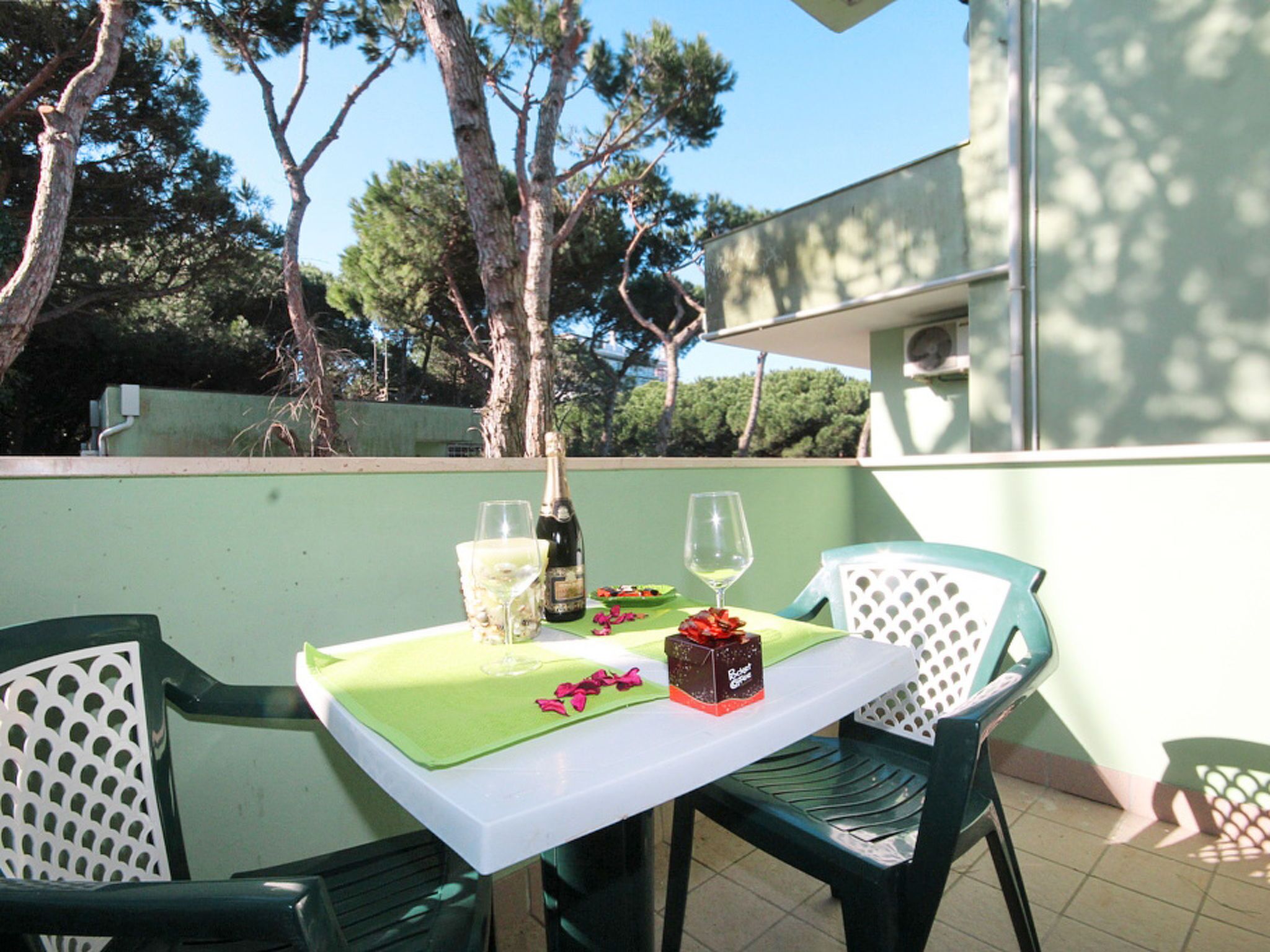 Patio esterno con tavolo apparecchiato per due, con una bottiglia di champagne, due calici e una scatola di dolci.