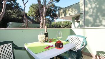 Patio esterno con tavolo apparecchiato per due, con una bottiglia di champagne, due calici e una scatola di dolci.