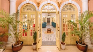 Un vaste hall d’entrée avec des portes en arc de cercle, un lustre et des plantes en pot.