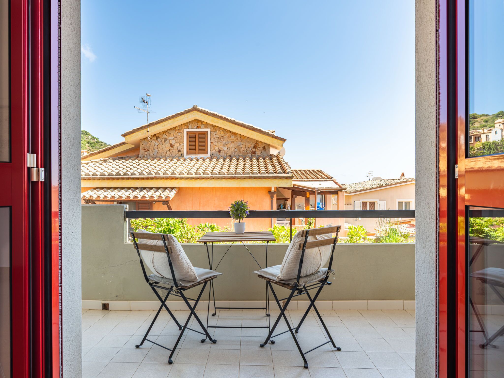 En balkon med to stole og et bord, med udsigt over en traditionel bygning i sten med tegltag.