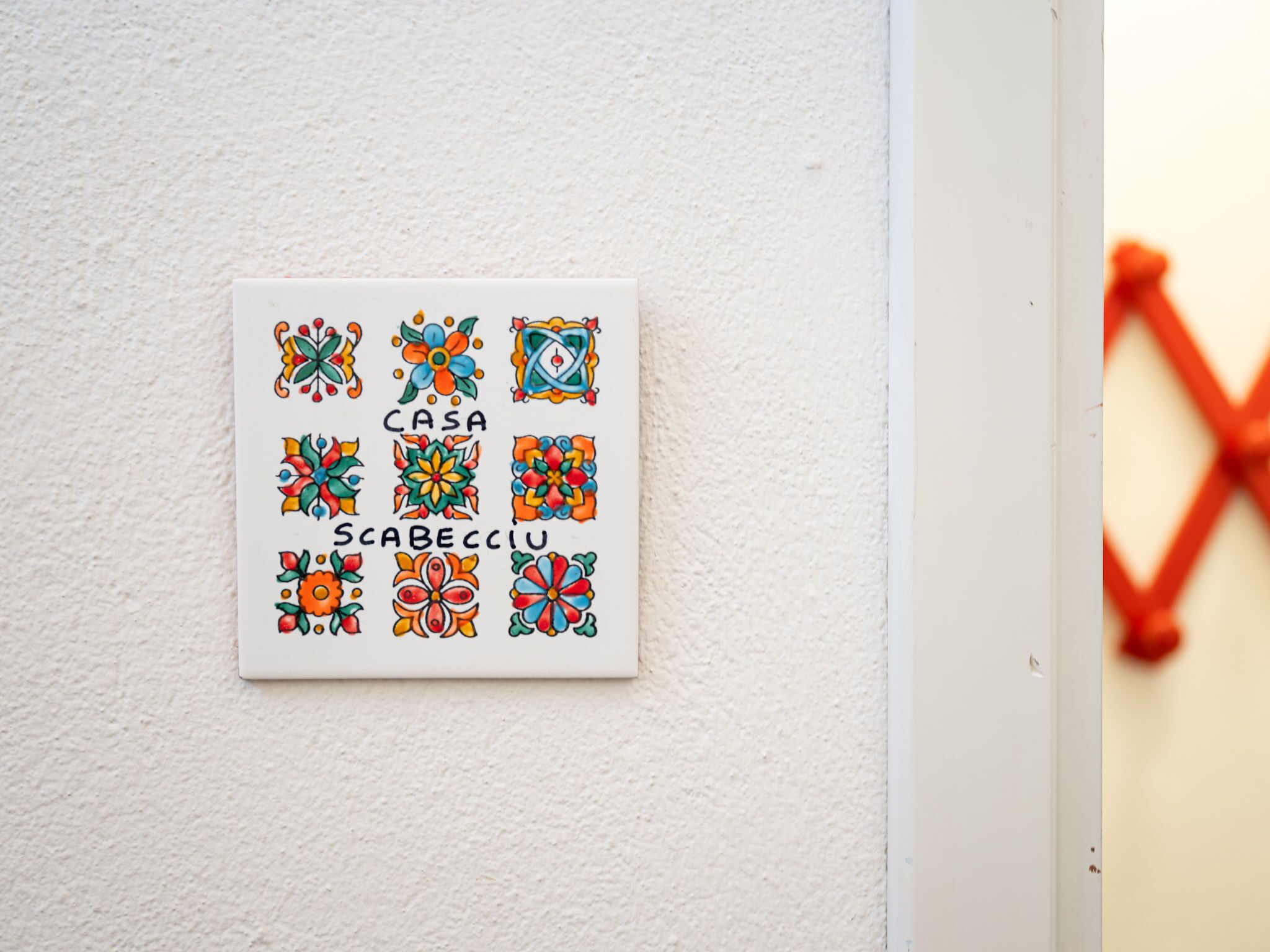 A white tile with colorful geometric patterns and the words "CASA" and "SCABECCIU" on it.