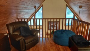 A cozy loft room with a wooden ceiling, a black leather chair, a blue bean bag, and a view of a snowy landscape through large windows. - Unique A-Frame wloft, pool, & RV electric 17 min from Silver Springs State Park  (Silver Springs)