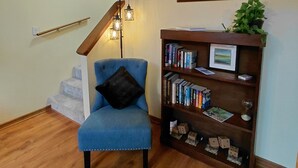 A living room with a blue armchair, a wooden bookshelf, a painting, and a staircase with wooden railings. - Unique A-Frame wloft, pool, & RV electric 17 min from Silver Springs State Park  (Silver Springs)