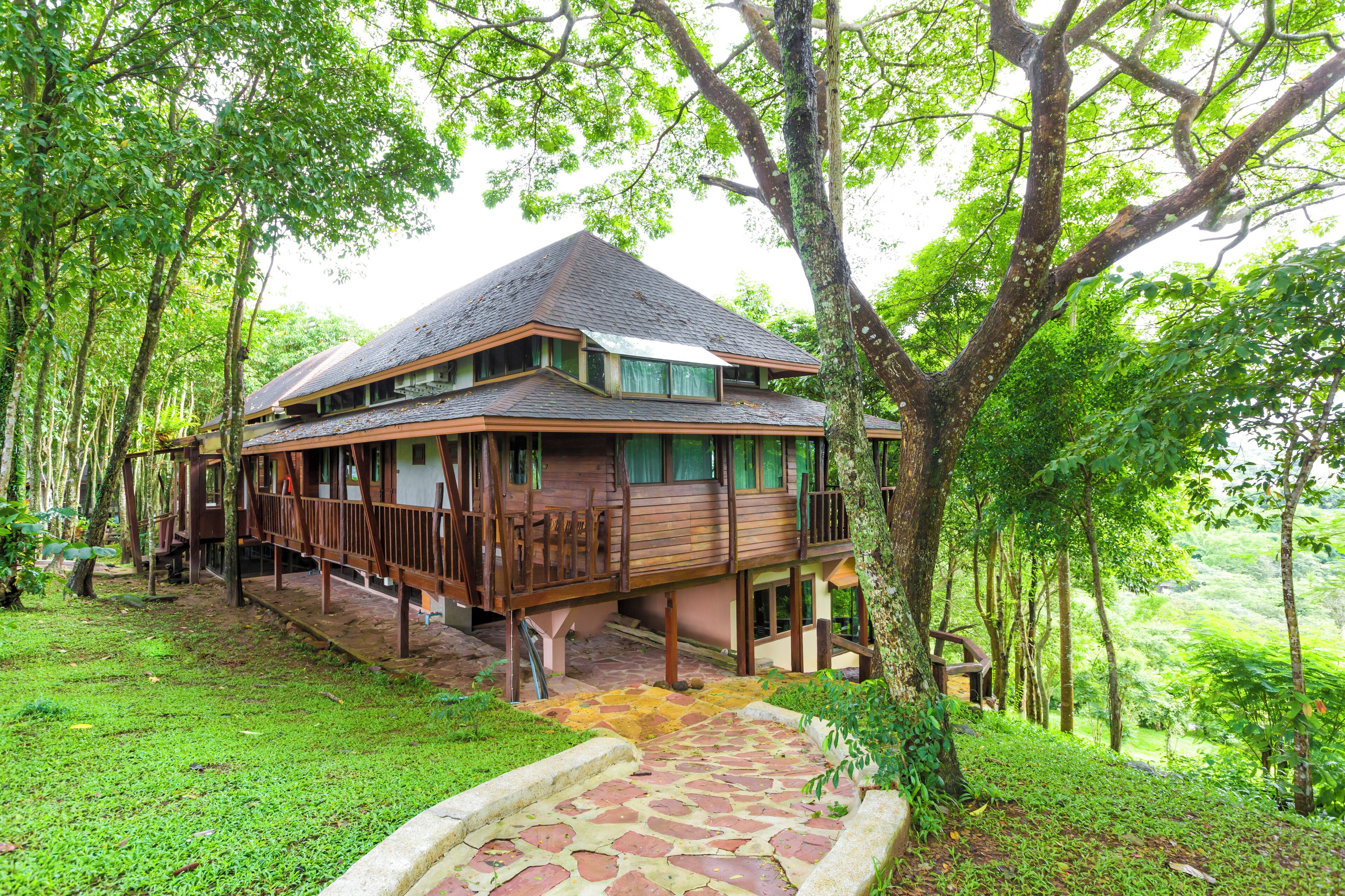 A wooden house with a balcony, surrounded by lush greenery and trees.