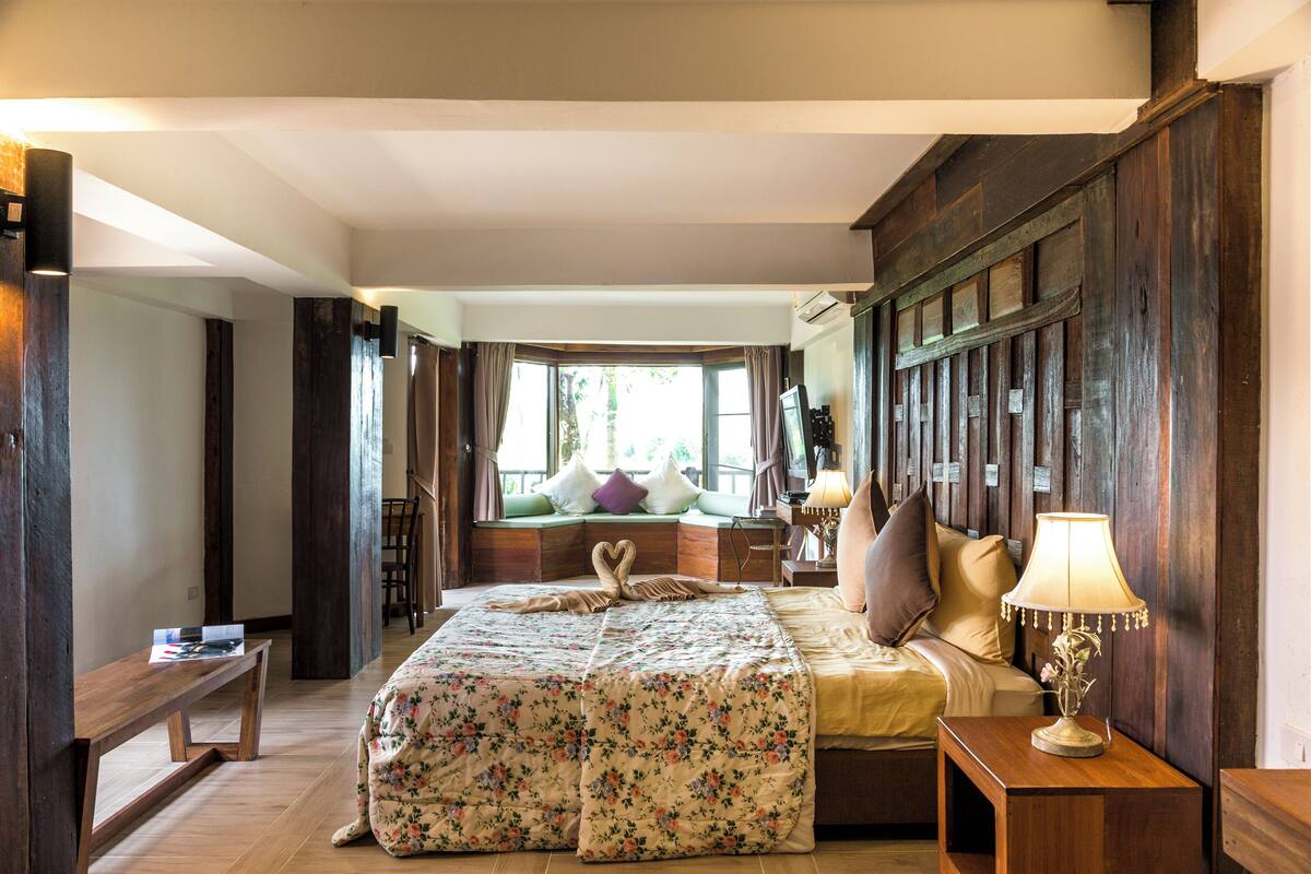 Un dormitorio con una cama grande, una mesita de noche con lámpara, una ventana con cortinas y vistas al exterior.
