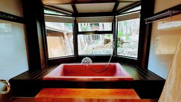 Een badkamer op hoek met een rood bad, een douche en uitzicht op een stenen muur en groen buiten.