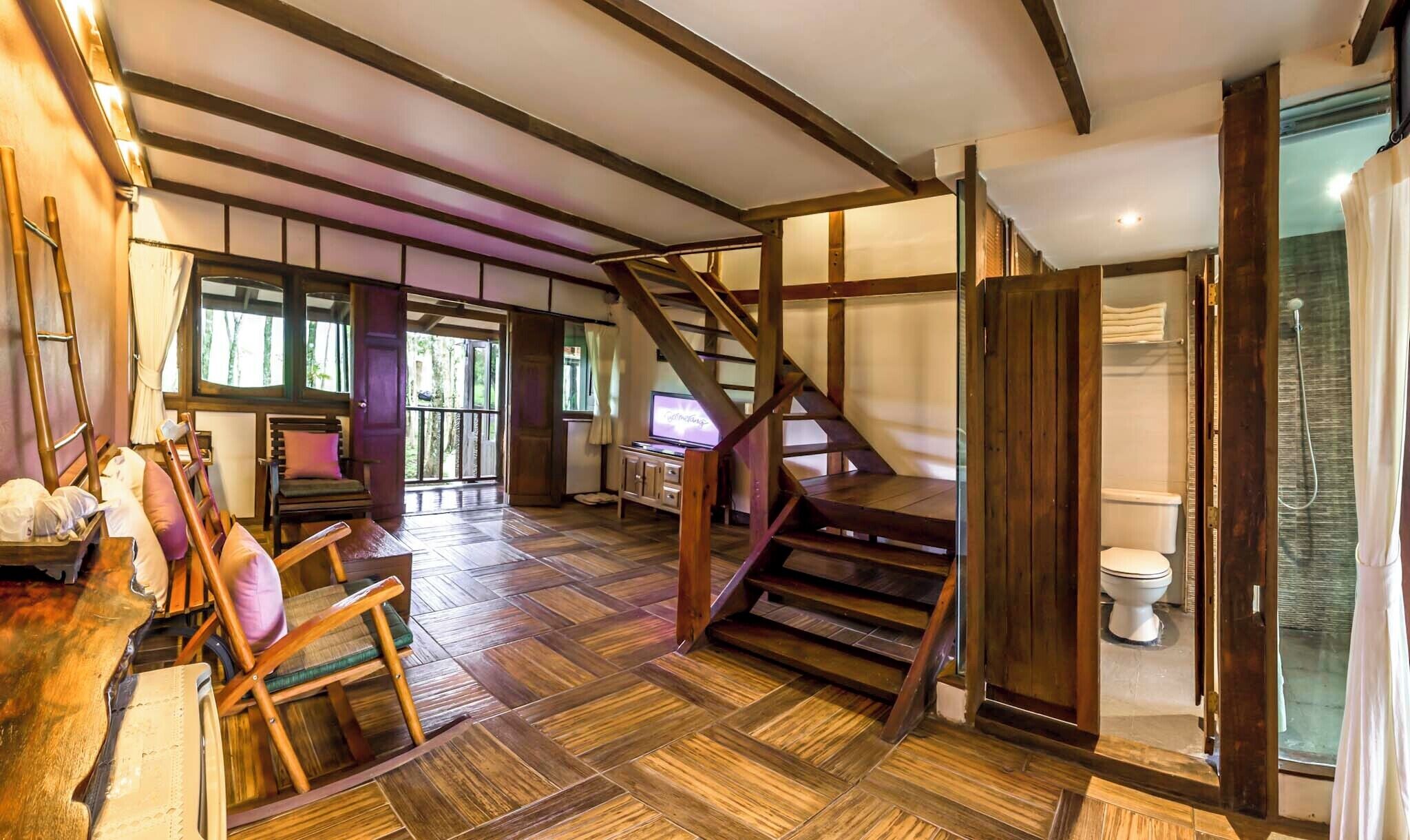 A spacious room with a herringbone floor, a wooden staircase, and a large window.