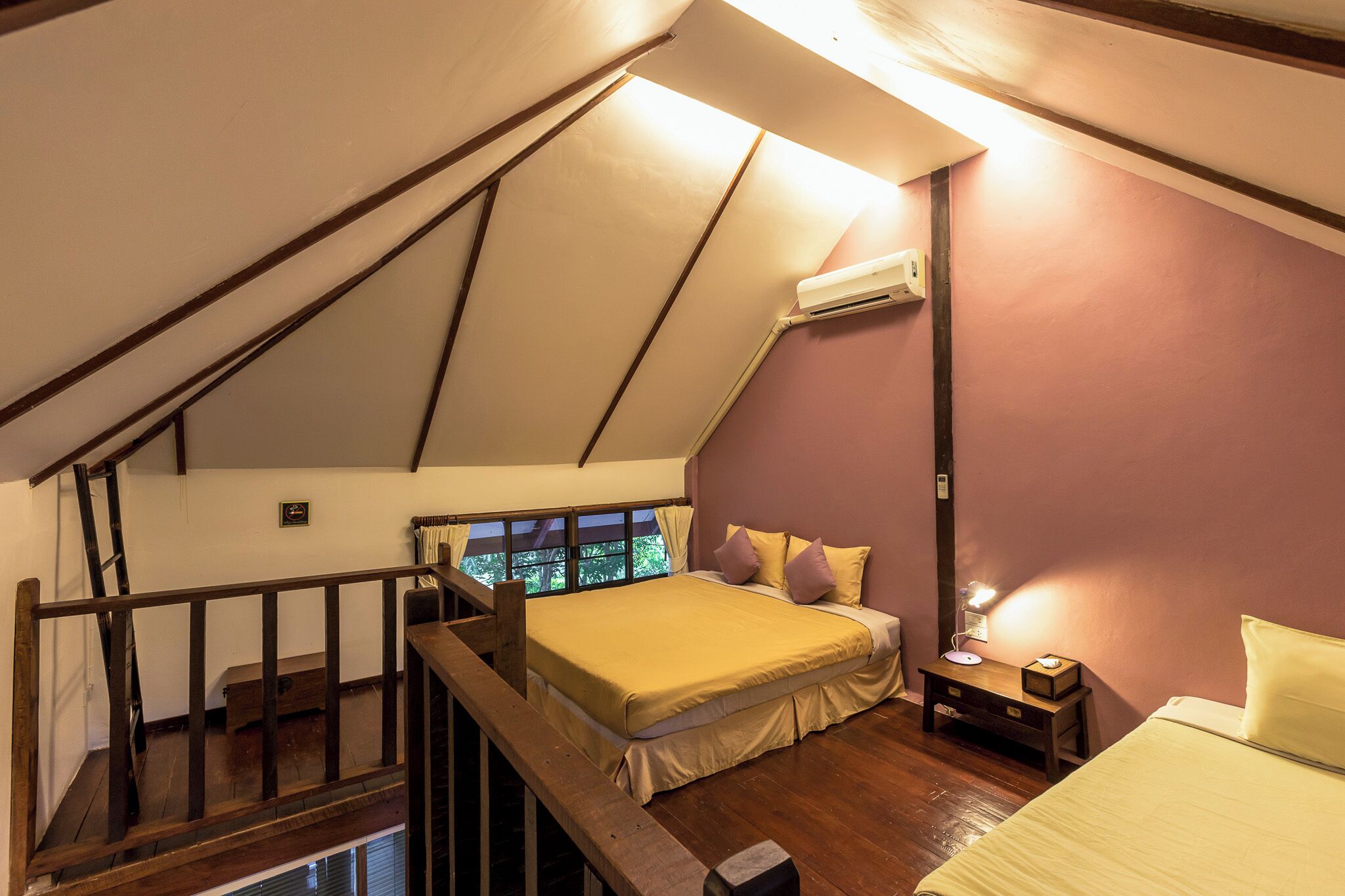 Een slaapkamer met een schuine kap, een bed met geel beddengoed, een nachtkastje met een lamp en een raam met gordijnen.