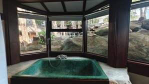 Un área de spa con una bañera grande, vigas de madera y vistas a un terreno rocoso al aire libre.