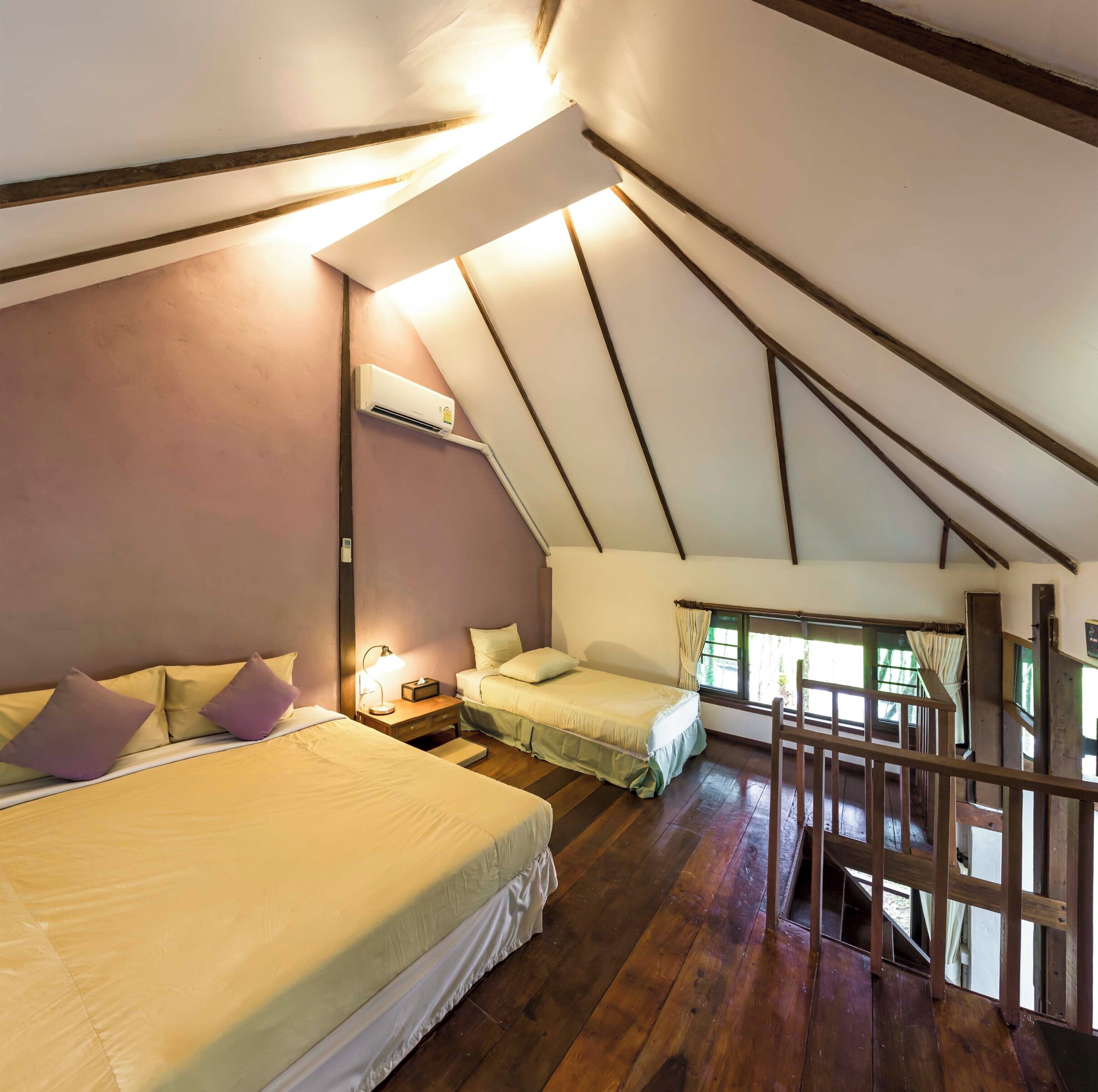 Une chambre confortable située dans les combles, avec deux lits, un escalier en bois et une fenêtre avec des rideaux.