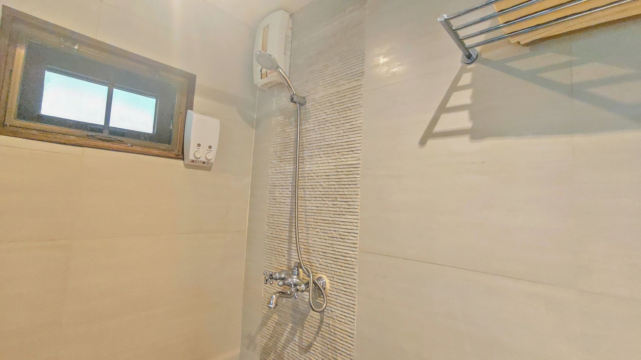 A shower with a handheld showerhead, a control panel, and a towel rack.