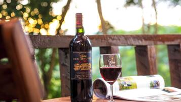 A bottle of wine and a glass on a wooden table with a magazine, set outdoors with a blurred natural background.