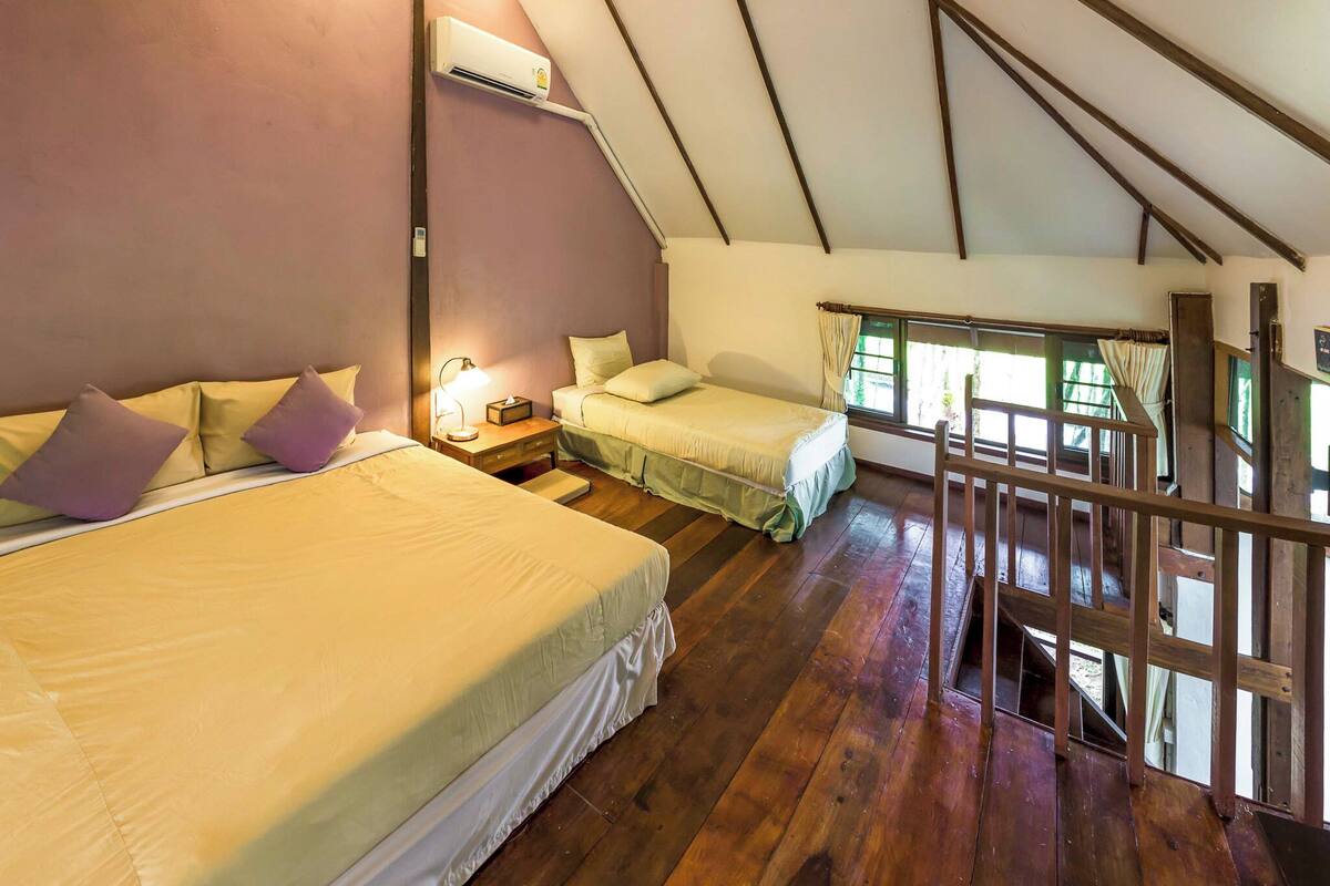 Un dormitorio acogedor en el ático con dos camas, una escalera de madera y una ventana con cortinas.