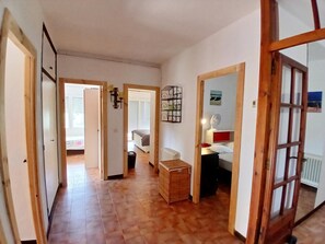 Un couloir avec un plancher en bois, un lit avec une tête de lit rouge, un radiateur blanc et un panier en osier.