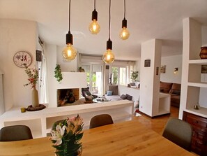 Een moderne woonkamer met een houten eettafel, een open haard en hangende lampen.