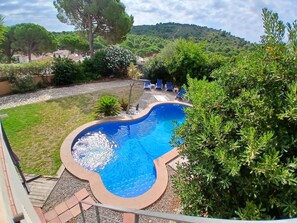 Une piscine entourée de verdure, avec vue sur une colline et quelques bâtiments en arrière-plan.