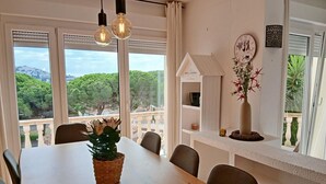 A dining area with a wooden table, chairs, hanging light bulbs, a decorative vase, and a view of greenery and buildings through large windows. - Holiday home with private pool in L'Escala. HUTG-011949 (l'Escala)