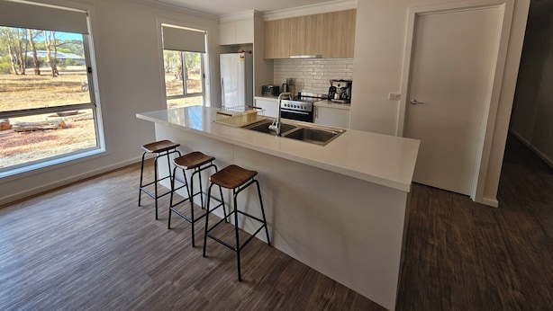 A modern kitchen with a large island, bar stools, and a view of the outdoors. - Pet Friendly Relax with the whole family or friends. (Axedale)