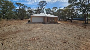 A small, single-story building with a flat roof, surrounded by trees and dry ground. - Pet Friendly Relax with the whole family or friends. (Axedale)