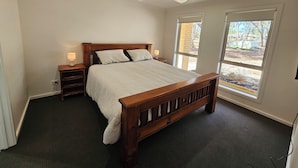 A bedroom with a wooden bed, two bedside tables with lamps, a ceiling fan, and large windows with a view of the outdoors. - Pet Friendly Relax with the whole family or friends. (Axedale)