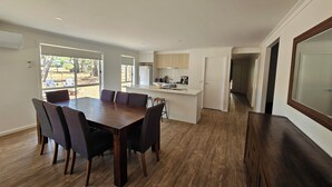 A modern kitchen with white cabinets, a central island, and a dining area with a wooden table and chairs. - Pet Friendly Relax with the whole family or friends. (Axedale)