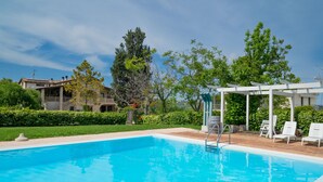 Une piscine d’un bleu éclatant, agrémentée d’une pergola blanche et de chaises longues.