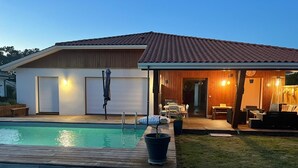A modern house with a swimming pool, a covered patio, and a well-lit interior. - House with swimming pool near Contis beach, cycle path and all amenities (Saint-Julien-en-Born)