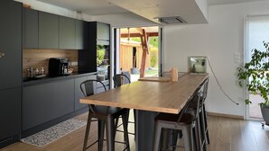 A modern kitchen with dark cabinets, a wooden island, and a view of the outdoors. - House with swimming pool near Contis beach, cycle path and all amenities (Saint-Julien-en-Born)