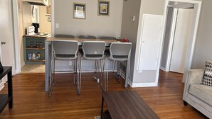 A dining area with a wooden table and four chairs, a kitchen with a microwave and coffee maker, and a sofa in the living room.