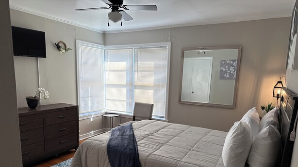 A bedroom with a bed, dresser, TV, and windows.