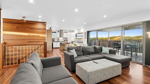Un espacio habitable amplio con un sofá seccional gris grande, un reposapiés estampado y una escalera de madera.