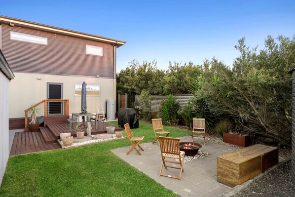 A backyard with a wooden deck, outdoor seating, a fire pit, and a barbecue grill.