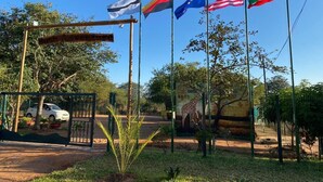 A fenced area with flags of various countries, a sign reading "Rich Adventures", and a giraffe enclosure. - Bush Adventure Guest House (Kasane)