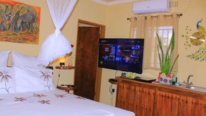 A hotel room with a bed, a television, a wooden cabinet, and a wall painting. - Bush Adventure Guest House (Kasane)