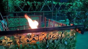 A fire burning on a bridge with a metal railing and greenery in the foreground.