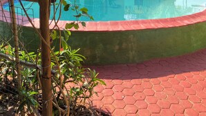 A swimming pool with a wooden deck, surrounded by greenery and a building with a green facade. - Bush Adventure Guest House (Kasane)