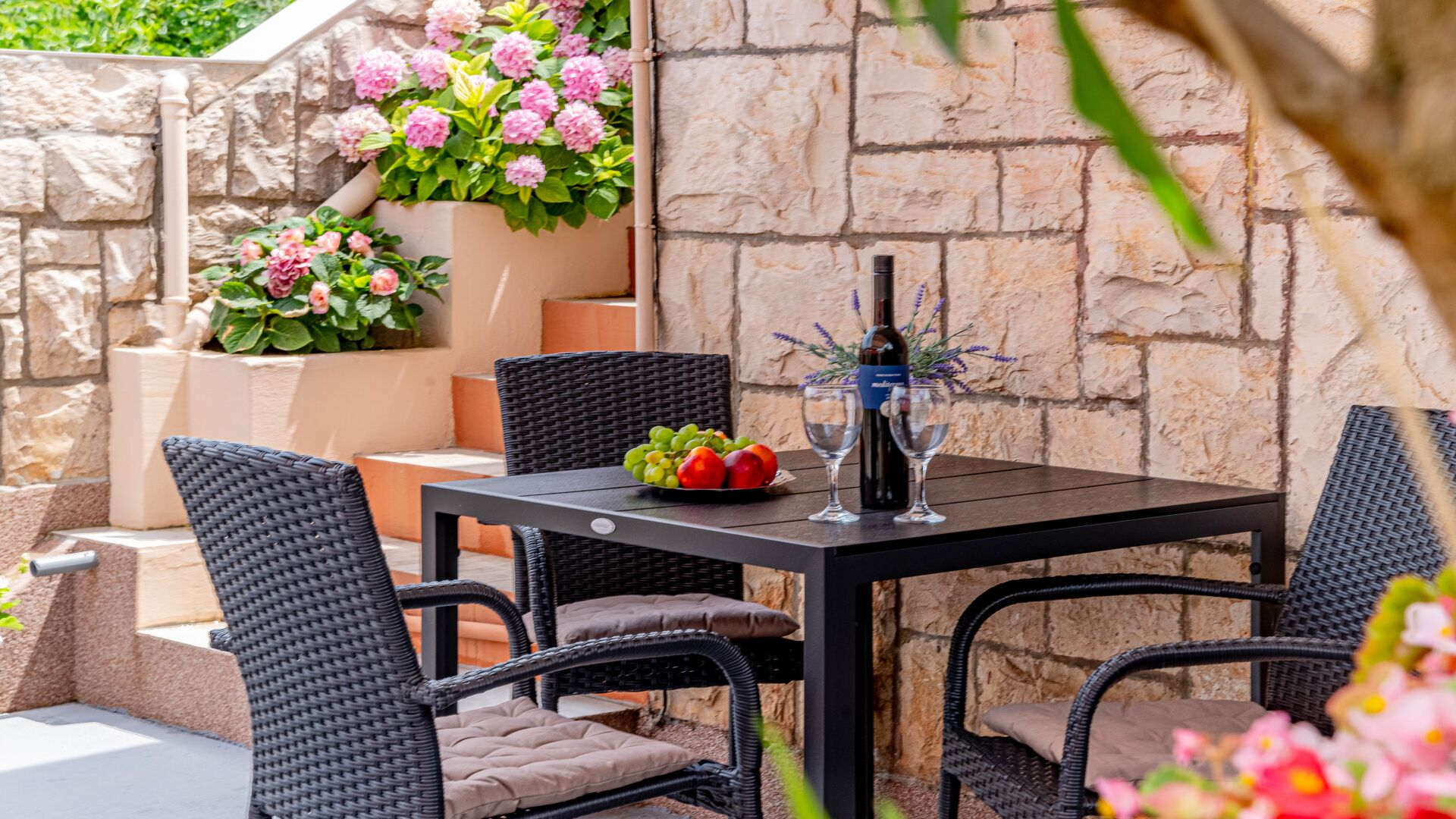 An outdoor patio with wicker chairs, a table, and a bottle of wine.