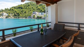 A balcony with a table, chairs, a bottle of champagne, and a view of a lake and buildings. - Villa Mustapic by Villas Guide (Blace)