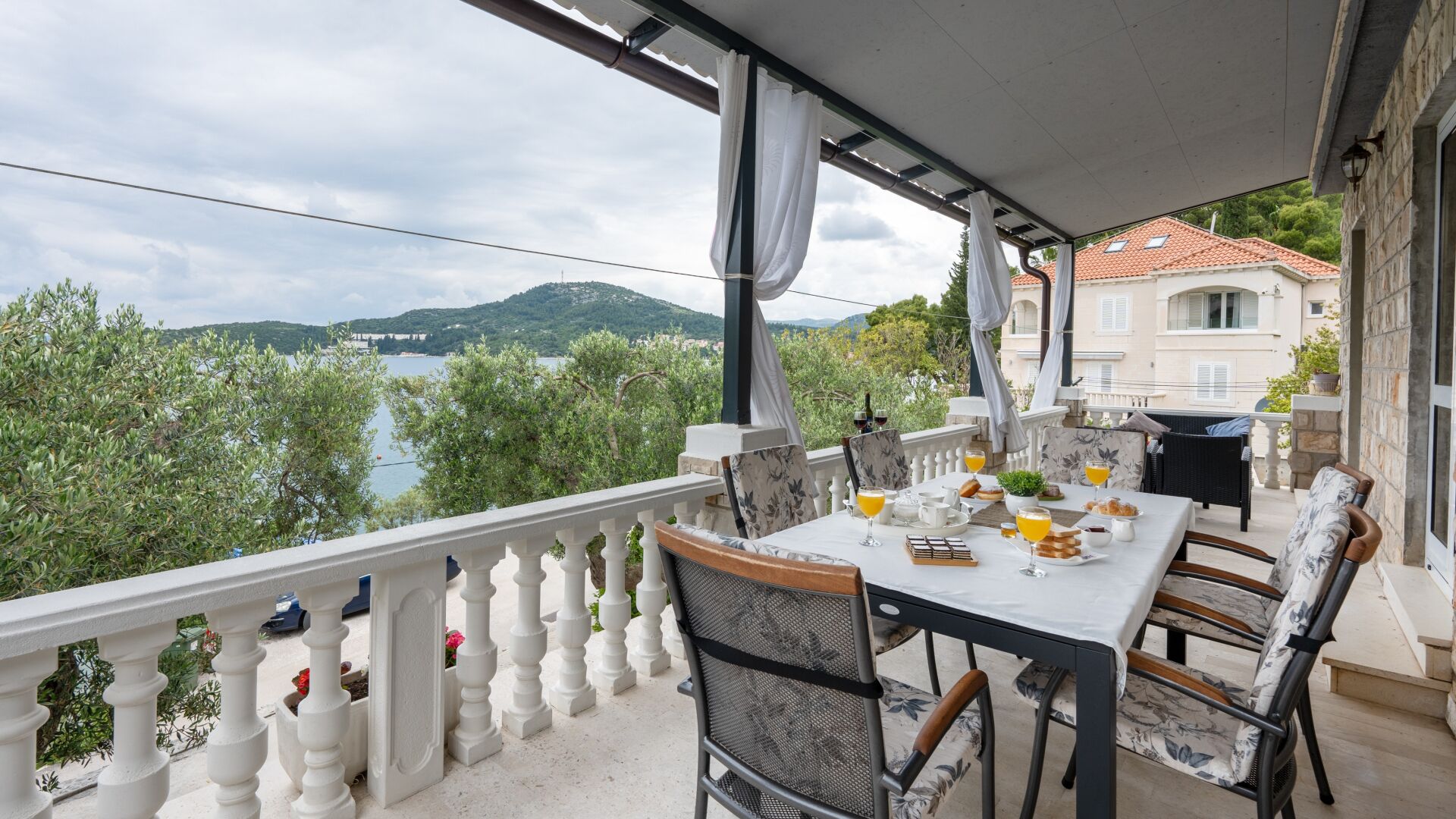 A balcony with a table set for breakfast, overlooking a lake and hills.