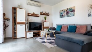 A modern living room with a grey sofa, a TV, a small round table, and decorative items on shelves. - Apartman Marija Slano by Villas Guide (Slano)