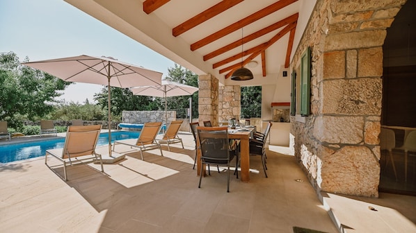 A poolside area with lounge chairs, a dining table, and umbrellas.