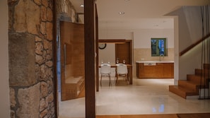 Un intérieur moderne avec un mur en pierre, un coin repas avec des chaises et une table, une cuisine avec des meubles en bois et un escalier.